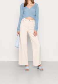 Maglione a maglia cropped blu chiaro, pantaloni a gamba larga bianchi sporchi e morbidi, borsa blu chiaro e sandali con tacco a blocco abbinati.