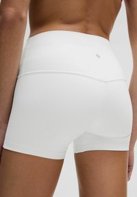 Pantalones cortos de rendimiento blancos con una textura suave, cintura alta y costuras planas para mayor comodidad. Logo de Lululemon exhibido en la parte trasera.