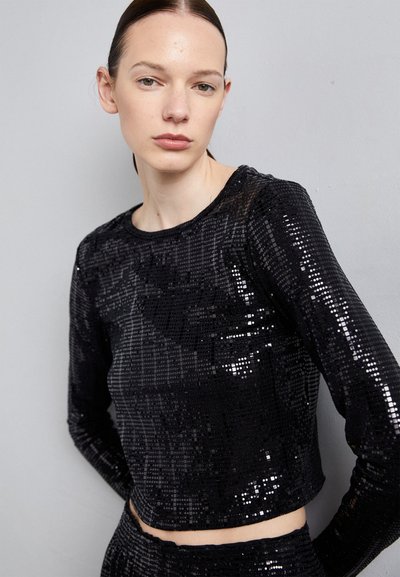 Melnas sequined garām piedurknēm blūze ar apaļu kakla izgriezumu un īsāku dizainu. Gluda tekstūra ar atstarotājiem visā audumā.