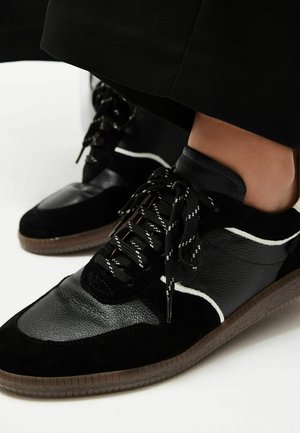 Sorte sneakers med en blanding af glat læder og ruskind, hvide accenter, strukturerede snørebånd og en brun gummisål.