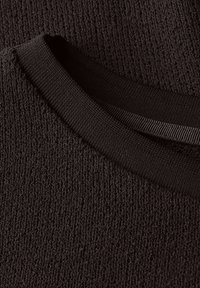 Czarna dzianina z teksturową powierzchnią, z jednolitym kołnierzem w nieco innym odcieniu czerni dla kontrastu.