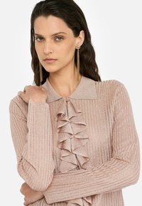 Rosa ribbad blus med knappad krage, med vertikala volanger fram. Långa ärmar med detaljerade manschetter och texturerad tyg.