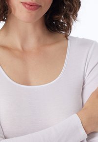Valkoinen pitkähihaisinen paita, jossa on pyöreä kaula-aukko, valmistettu pehmeästä ribbikäytöstä. Suhli tekstuuri hienovaraisella joustavuudella, jossa on minimaalinen ompelu.