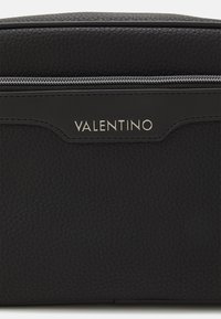 Svart lærpung med teksturert overflate, med sølvfargede detaljer og en diskret "VALENTINO"-logo på framsiden. Glidelås på toppen.