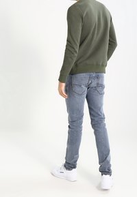 Suéter de textura verde oliva con puños y dobladillo acanalados, combinado con jeans ajustados de color azul claro y zapatillas blancas con un sutil logotipo.