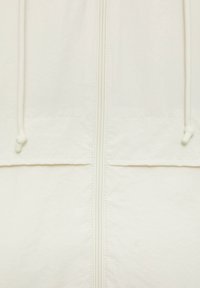 Veste blanche légère dotée d'une fermeture éclair à l'avant et d'une capuche avec cordon, texture lisse, et deux poches basses. Design simple avec des détails minimalistes.