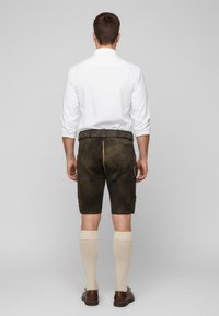 Braune Lederbermuda mit glatter Textur, einem Bund und einer seitlichen Tasche, kombiniert mit cremefarbenen kniefreien Socken und braunen Schuhen.