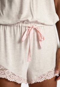 Pantalones cortos de punto gris claro con un lazo de satén rosa en la cintura y un acabado de encaje que presenta patrones florales a lo largo del dobladillo.