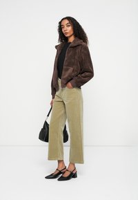 Bruine fuzzy jas, zwarte top, groene wijde corduroybroek, zwarte handtas en zwarte hoge hakken. Krullend haar losgestyled.