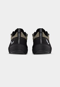 Ζευγάρι μαύρα και ελαιδί παπούτσια για τρέξιμο στο μονοπάτι, ορατά από πίσω, με λωρίδες τραβήγματος που φέρουν λευκό κείμενο και λογότυπα εμπορικών σημάτων στις φτέρνες.