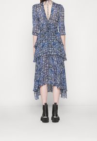 Vestido azul con estampado, de manga tres cuartos, con volantes escalonados y un escote profundo en la espalda. Combinado con botas negras hasta el tobillo.