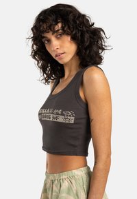Grå rutad crop top med rund halsringning och en tryckt logotypdesign i mitten. Matchad med ljusgrön mönstrad byxor.