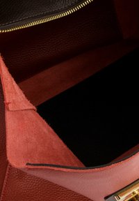 Red leather handbag interior featuring smooth and suede textures, with a gold zipper and a contrasting black bottom.
