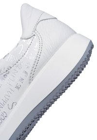 Weißer Leder-Sneaker mit Fersendetail aus silbernem Glitzertext und grauer, profilierter Gummisohle.