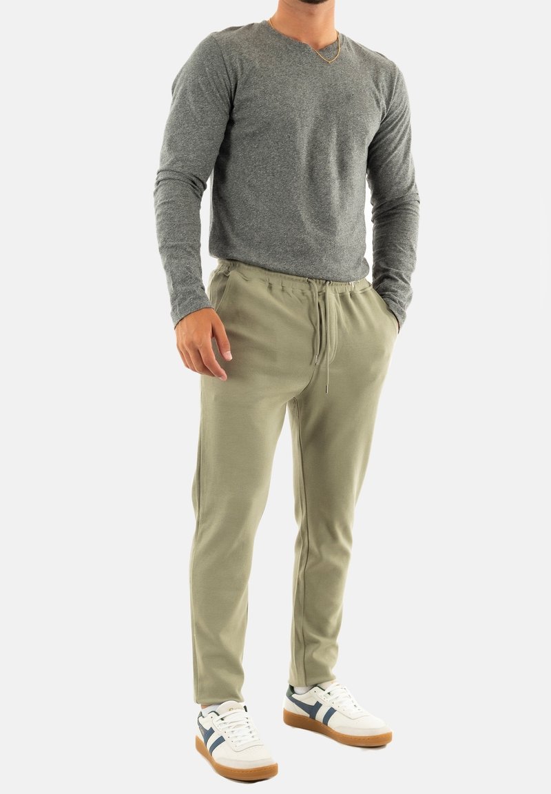 Grijze long-sleeve shirt, olijfgroene sweatpants met trekkoord, en witte sneakers met marineblauwe en tan accenten. Eenvoudig ontwerp en zachte textuur.