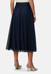 Jupe en tulle bleu marine avec une silhouette ample, dotée d'une taille solide et de couches fluides qui ajoutent de la texture. Portée avec des talons beiges.