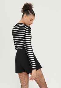 Haut à manches longues rayé noir et blanc associé à un short noir et des collants en résille, mettant en avant une texture côtelée et un design ajusté.