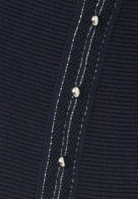 Close-up van donkerblauwe geribbelde stof met een textuurlint met drie glanzende zilveren knopen en lichtreflecterende stiksels.