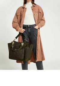 Nylon tote taske i mørkegrøn med en quiltet forlommetaske, med dobbelt bærerem og justerbar skulderrem. Matchet med en lang, pink jakke.