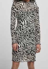 Černobílé dlouhé šaty s dlouhým rukávem, zdobené vzorem zebra, vyrobené z poloprůhledného materiálu a s rýhovaným lemem.