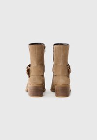 Bottes chelsea en daim marron avec un talon épais à nervures, des fermetures éclair sur les côtés et une sangle décorative avec un accent en métal.