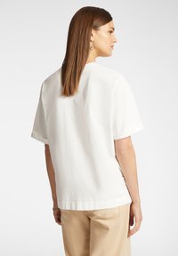 T-shirt bianca in cotone con maniche corte e una vestibilità leggermente ampia, con orlo dritto e scollo rotondo. Design minimalista senza fantasie.