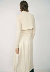 Ribbed cream sweater with a cropped back, paired with a flowy, pleated ivory skirt. Smooth texture and relaxed silhouette.