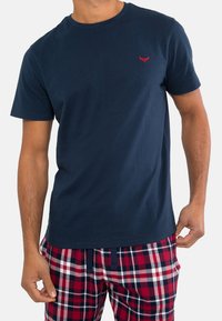 Marineblauw katoenen T-shirt met een ronde hals en korte mouwen, voorzien van een klein rood logo op de borst. Draag het met rode en witte geruite pyjamabroek.