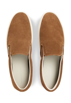 Par brune ruskind slip-on sko med hvide gummisåler, set ovenfra på hvid baggrund.