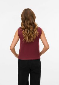 Burgundy ärmlös topp med en slät yta, rundad halsringning och en figurnära silhuett, kombinerad med högmidjade svarta byxor.