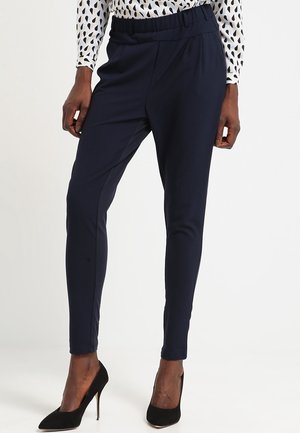 Pantalons ajustés bleu marine avec un design fuselé, une taille élastique, un tissu doux et des poches avant, associés à des talons hauts noirs.