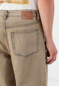 Beige farmernadrág, hátoldali zsebbel, kontrasztos varrással, bőr címkével az "element" márkázással és laza szabással.