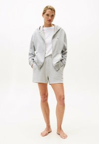 Felpa grigia con tasche anteriori e zip, abbinata a pantaloni corti grigi coordinati. Il tessuto è morbido e il design è semplice con una vestibilità comoda.