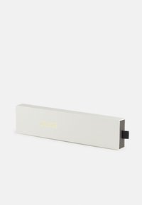 Boîte rectangulaire de couleur gris clair avec une surface texturée. Présente un logo doré "CLUSE" sur le devant et une languette noire d'un côté.