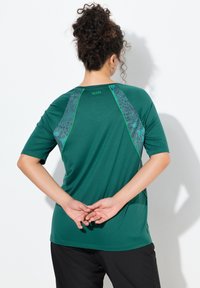 Zelené tričko s krátkým rukávem a šedými vzorovanými akcenty; má kulatý výstřih a kontrastní zelený lem podél ramen a zad.
