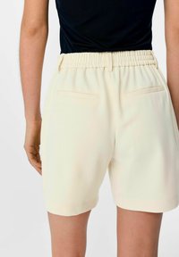 Crème-kleurige shorts van zachte stof met een elastische tailleband en twee achterzakken. Heeft een losse pasvorm en een rechte pijpdesign.