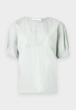 Jasnoszara bluzka z krótkim rękawem i okrągłym dekoltem o subtelnej fakturze. Charakteryzuje się luźnym krojem i lekko bufkami na rękawach dla swobody ruchów.