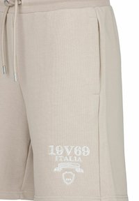 Beige katoenen shorts met elastische tailleband, trekkoord en zijzakken. Witte geborduurde logo-details op het onderbeen.