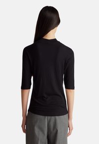 Černý žebrovaný top s krátkým rukávem a vysokým límcem, s přiléhavým střihem a bezšvou zadní částí. V kombinaci se šedými kalhotami.