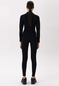 Zwart sportset met een getailleerde lange mouwen top en hoge taille legging, gemaakt van glad, rekbaar materiaal; minimalistisch ontwerp, geen patronen.