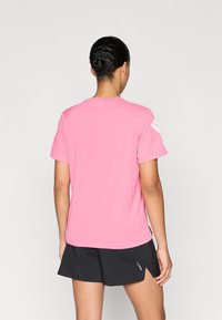 Ροζ κοντομάνικο μπλουζάκι με στρογγυλή λαιμόκοψη και μανίκια ράγκλαν. Μαύρο αθλητικό σορτς με πλευρική σχισμή. Απλός σχεδιασμός, λεία υφή.