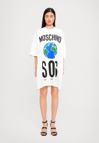 Abito t-shirt oversize bianco con grafica della Terra in blu e verde, testo bold in nero che recita "MOSCHINO" e "SOS," con una texture liscia.