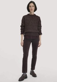 Bordeauxfarbener Strickpullover mit Rundhalsausschnitt, kombiniert mit dunkelburgunderfarbenen Cordhosen. Die Schuhe sind braun mit Fransenverzierungen. Glatter, strukturierter Sitz.