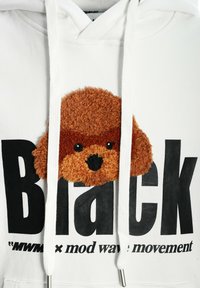 Sudadera blanca con un aplique de perro marrón de felpa en el pecho. Texto grande en negro que dice "Black" con texto más pequeño debajo.