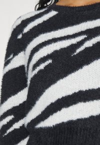 Gros plan d'une personne portant un pull tricoté à rayures zébrées en noir et blanc, doux et à encolure ronde.