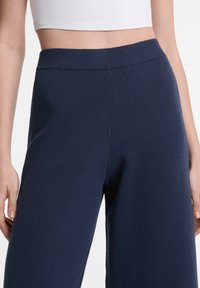 Marineblaue weite Hose aus einem strukturierten, weichen Stoff. Sie verfügt über einen gerippten Bündchen und eine lockere Passform, die ideal für Komfort und Bewegungsfreiheit ist.