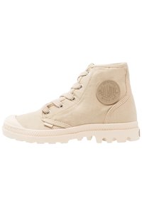 Beige vysoké plátěné boty s gumovou špičkou, texturovaná látka, kovové očko a značková kruhová nášivka na boku.