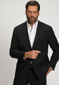 Zwarte pakken met een enkele knoopsluiting, een textuurstof en een wit overhemd met kraag. Hand gepositioneerd en wijzend, met een rode accent.