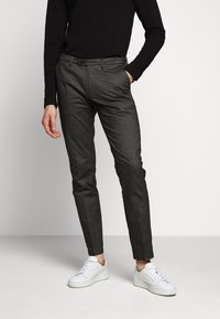 Pantaloni grigi su misura con una vestibilità slim, tessuto textured, passanti per cintura e tasche laterali, abbinati a sneakers bianche e una maglietta nera a maniche lunghe.