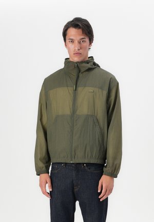 Oliven grønn zip-up jakke med hette, med en glatt, lett tekstur, doble brystlommer, og elastiske mansjetter og kant.